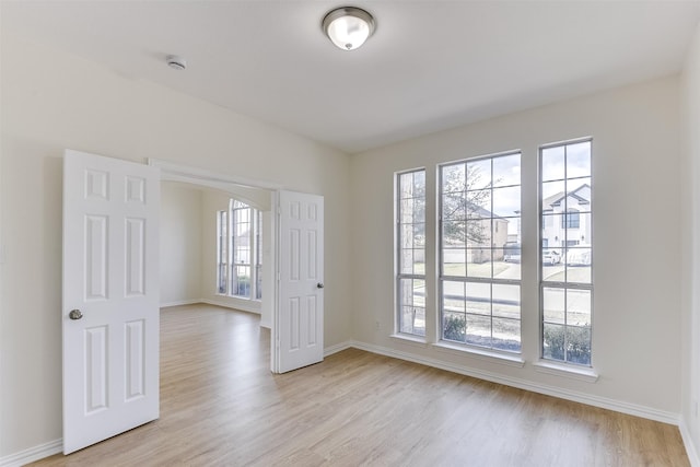 spare room with baseboards, arched walkways, and light wood finished floors