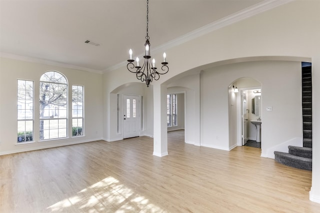 interior space featuring arched walkways, crown molding, light wood finished floors, a chandelier, and stairs