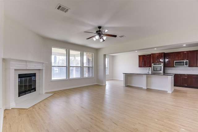 unfurnished living room featuring a sink, visible vents, ceiling fan, and light wood finished floors