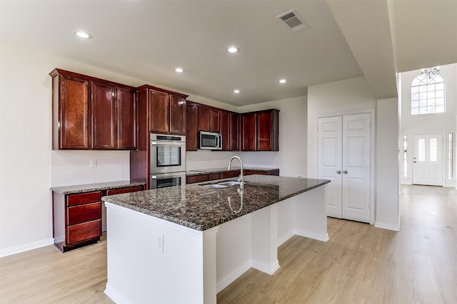 kitchen featuring light wood finished floors, visible vents, dark stone countertops, stainless steel appliances, and a sink