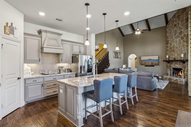 kitchen featuring gray cabinets, custom range hood, open floor plan, stainless steel appliances, and arched walkways