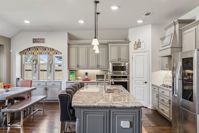 kitchen with visible vents, backsplash, light stone countertops, stainless steel appliances, and a sink