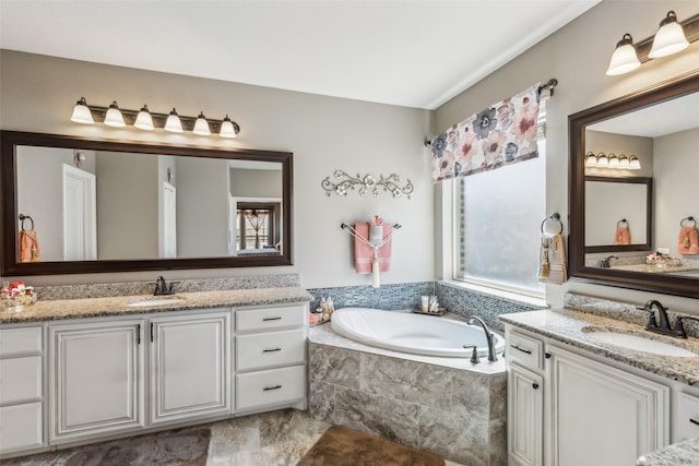 bathroom featuring a garden tub, two vanities, and a sink