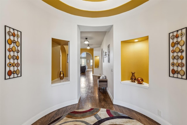 corridor with wood finished floors, baseboards, and arched walkways