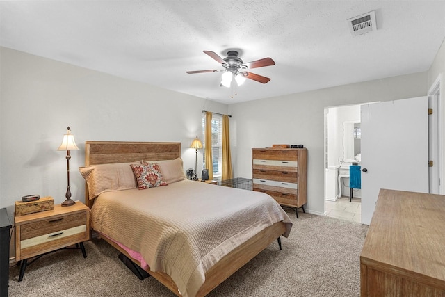 bedroom with visible vents, light colored carpet, ensuite bathroom, a textured ceiling, and a ceiling fan