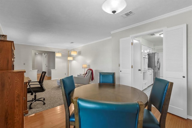 dining room featuring visible vents, light wood-style flooring, baseboards, and ornamental molding