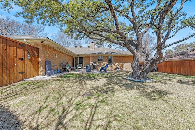 rear view of property featuring brick siding, fence, a lawn, a chimney, and a patio area