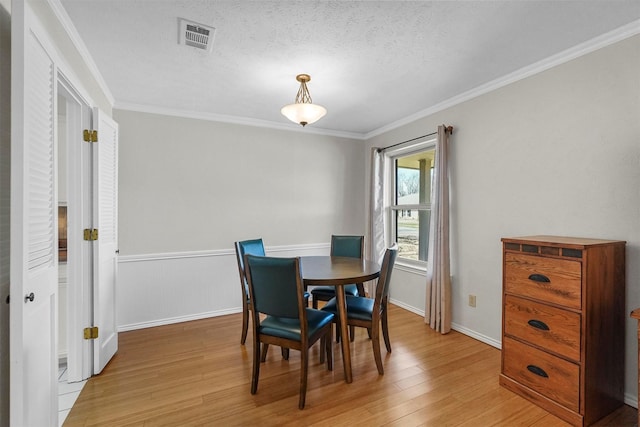 dining area with visible vents, baseboards, light wood-style floors, and ornamental molding