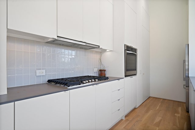 kitchen featuring light wood finished floors, white cabinets, under cabinet range hood, appliances with stainless steel finishes, and tasteful backsplash