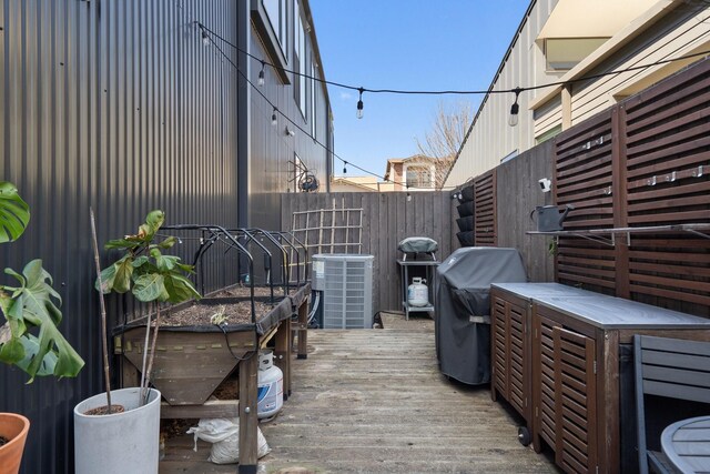 wooden deck featuring a grill, cooling unit, and fence