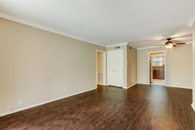 empty room with crown molding, baseboards, visible vents, and dark wood-style flooring