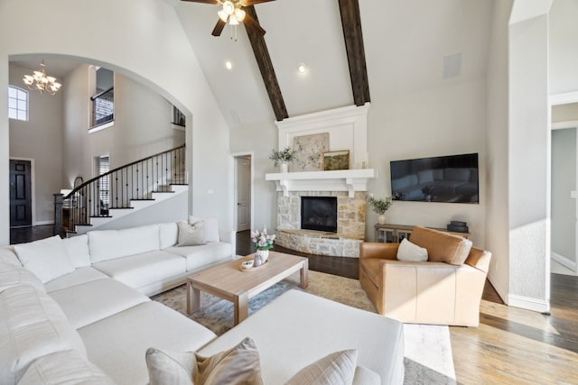 living room with wood finished floors, baseboards, high vaulted ceiling, a stone fireplace, and a notable chandelier