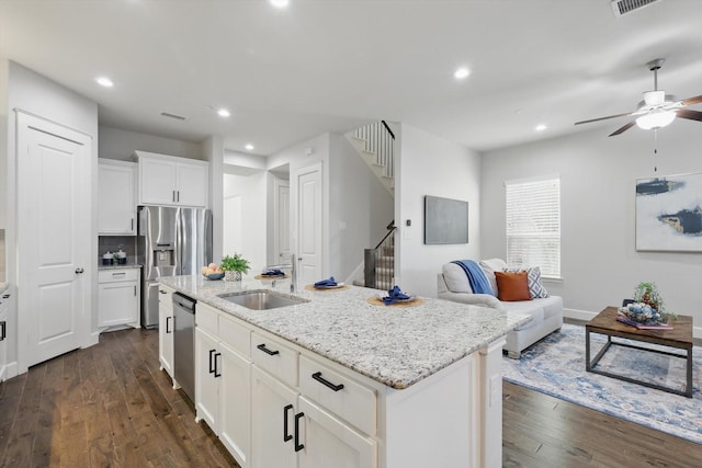 kitchen with light stone countertops, a center island with sink, dark wood-style floors, stainless steel appliances, and a sink