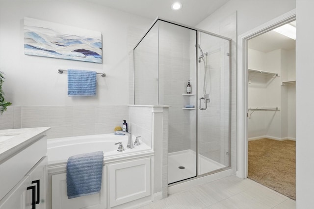 bathroom with tile patterned floors, a walk in closet, a stall shower, a bath, and vanity