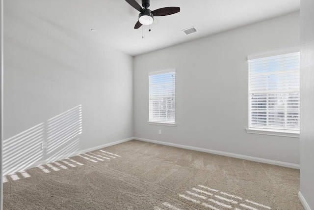 carpeted spare room featuring visible vents, a ceiling fan, and baseboards