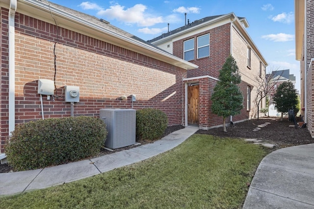 view of side of property featuring brick siding, central AC unit, and a yard