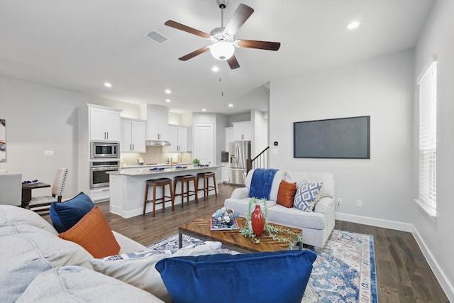 living area with dark wood finished floors, visible vents, ceiling fan, and baseboards