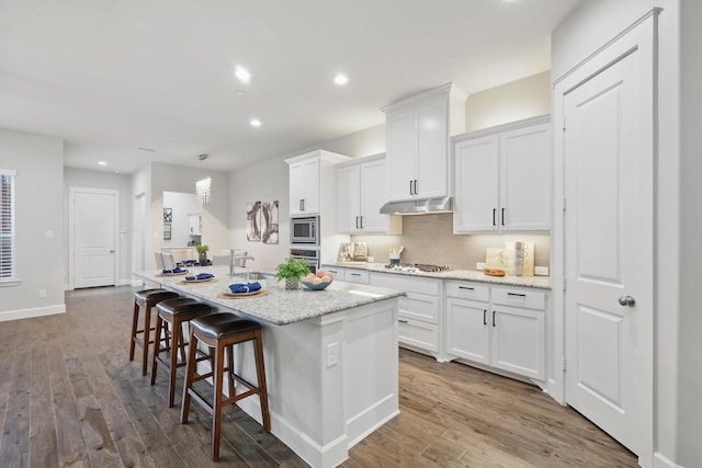 kitchen with a center island with sink, under cabinet range hood, a sink, white cabinetry, and appliances with stainless steel finishes