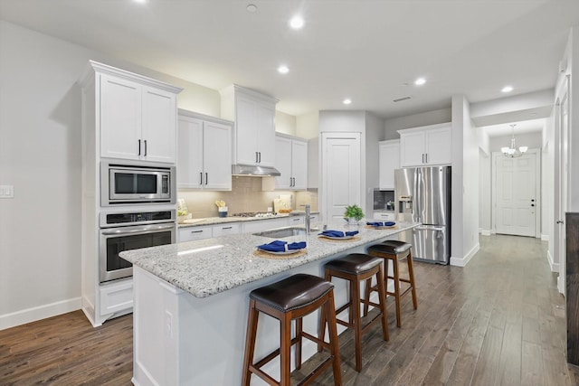 kitchen with under cabinet range hood, a sink, stainless steel appliances, a breakfast bar area, and decorative backsplash