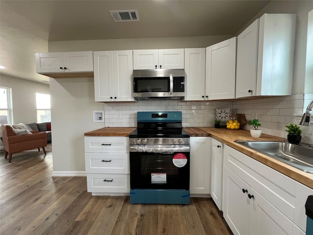 kitchen with wood finished floors, visible vents, a sink, appliances with stainless steel finishes, and wood counters