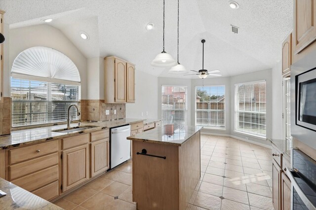 kitchen featuring light brown cabinets, dishwasher, lofted ceiling, light stone counters, and a sink