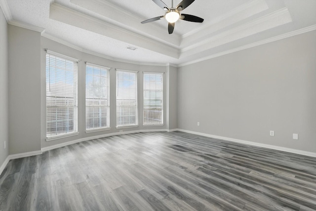 empty room with dark wood finished floors, baseboards, a tray ceiling, and ornamental molding