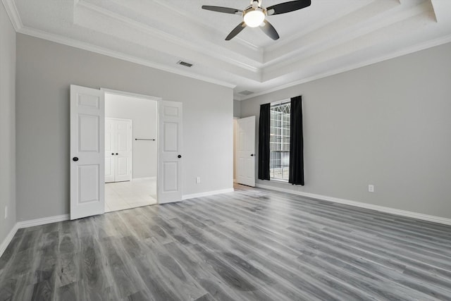 unfurnished bedroom with baseboards, crown molding, a tray ceiling, and wood finished floors