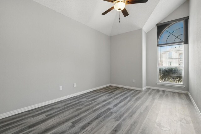 spare room with wood finished floors, a ceiling fan, baseboards, and vaulted ceiling