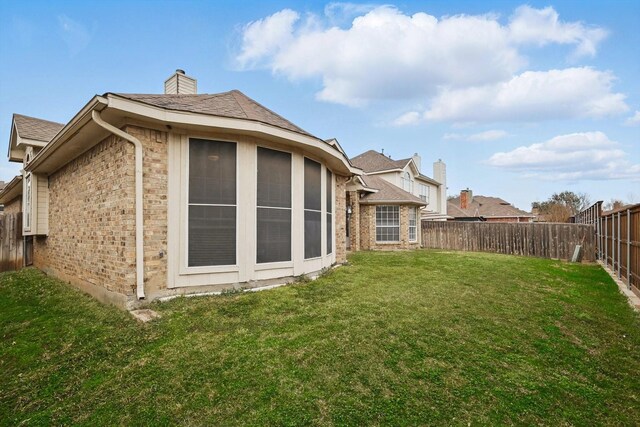 rear view of property featuring a yard, a fenced backyard, brick siding, and a chimney