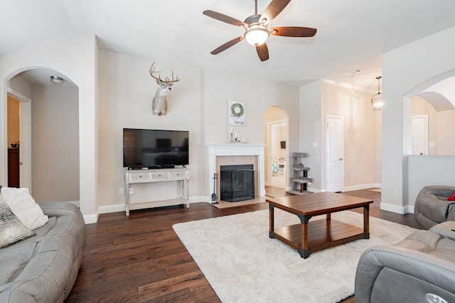 living area with baseboards, ceiling fan, dark wood-style flooring, and a tiled fireplace