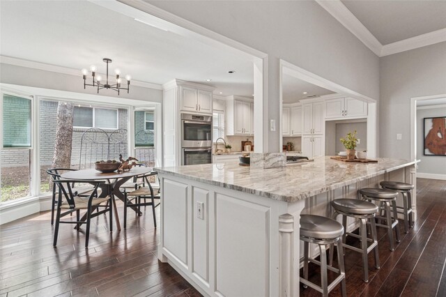 kitchen with light stone countertops, double oven, ornamental molding, an inviting chandelier, and dark wood-style flooring