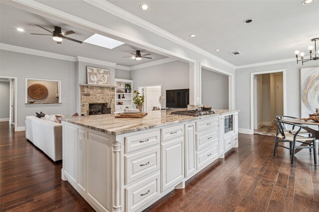 kitchen with light stone counters, a stone fireplace, dark wood-type flooring, appliances with stainless steel finishes, and open floor plan