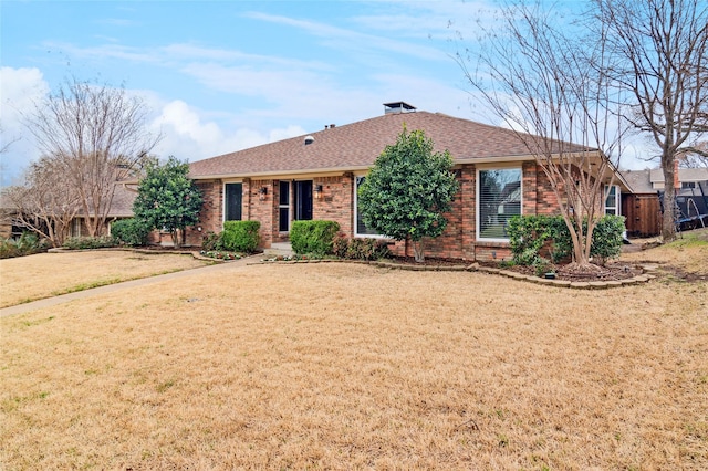 ranch-style house featuring a front yard, fence, brick siding, and roof with shingles