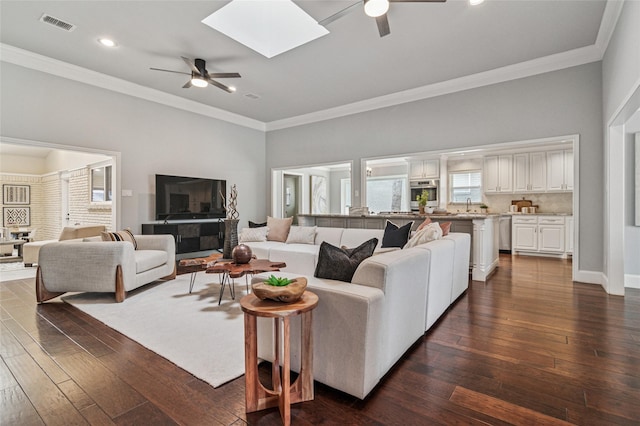 living area featuring dark wood finished floors, crown molding, and a skylight