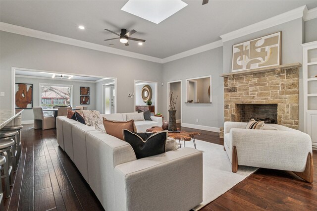 living area with baseboards, a skylight, a stone fireplace, dark wood-type flooring, and crown molding