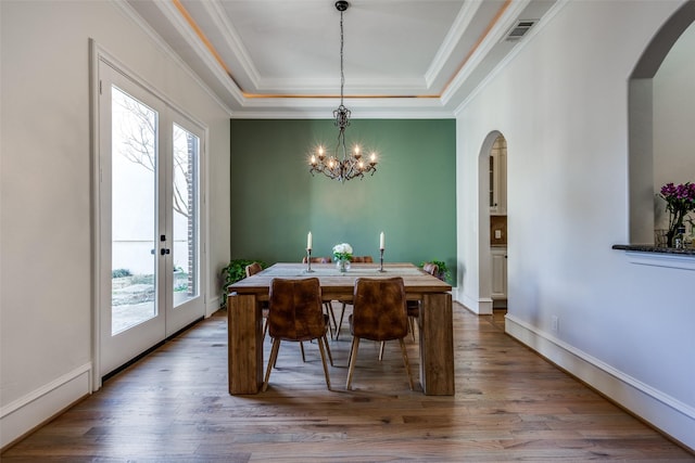 dining room featuring visible vents, arched walkways, a raised ceiling, and wood finished floors