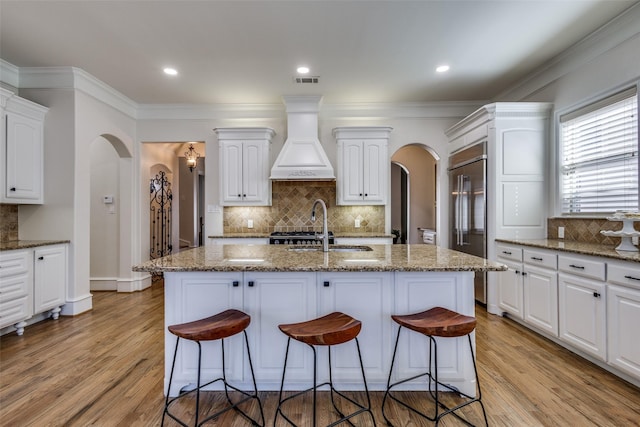 kitchen with a sink, arched walkways, custom exhaust hood, and a breakfast bar