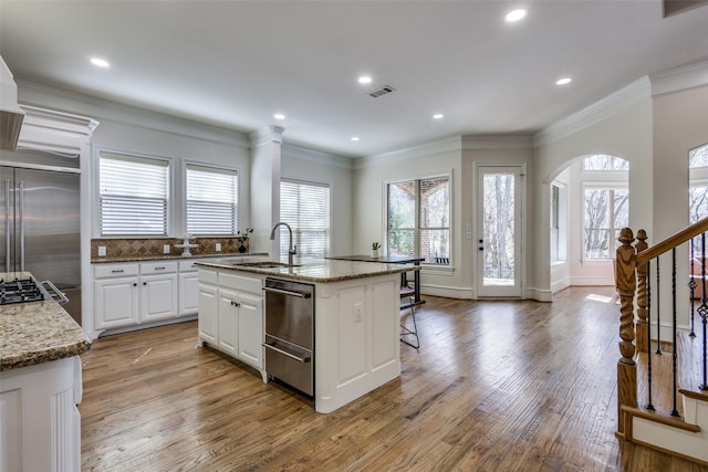 kitchen with a center island with sink, visible vents, a sink, built in fridge, and light wood-type flooring