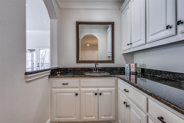 interior space with crown molding, white cabinets, dark stone countertops, and a sink