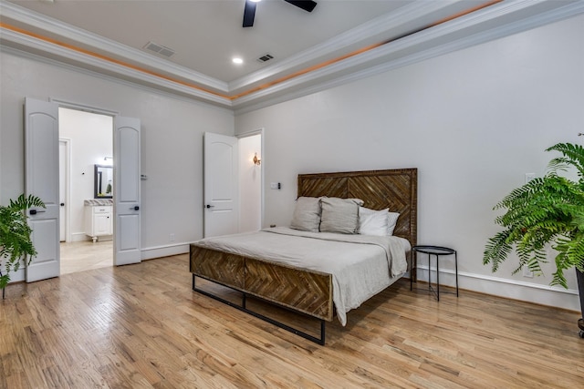 bedroom with a tray ceiling, visible vents, light wood-style flooring, and crown molding