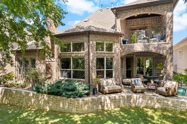 rear view of property featuring brick siding, a chimney, and a balcony