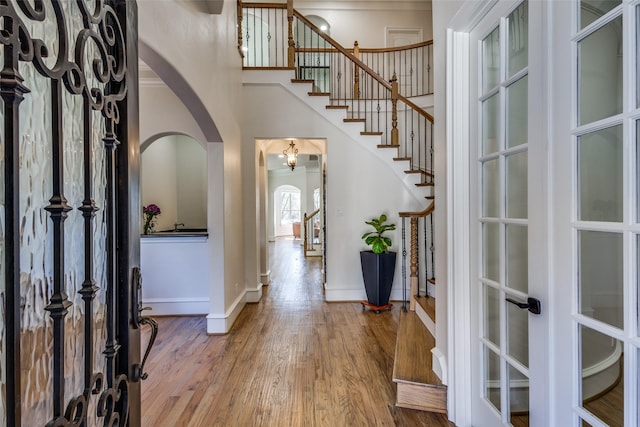 entryway featuring baseboards, stairway, a high ceiling, wood finished floors, and arched walkways