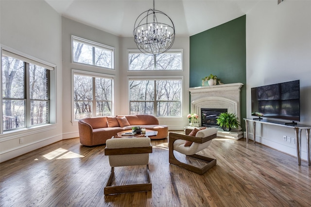 living room with a glass covered fireplace, wood finished floors, an inviting chandelier, baseboards, and a towering ceiling