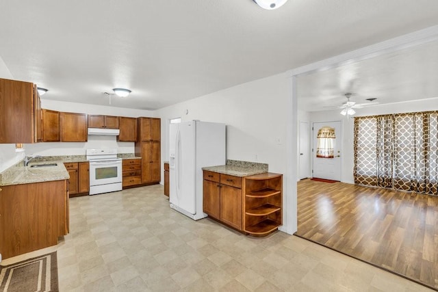 kitchen with brown cabinets, a sink, light stone counters, white appliances, and light floors