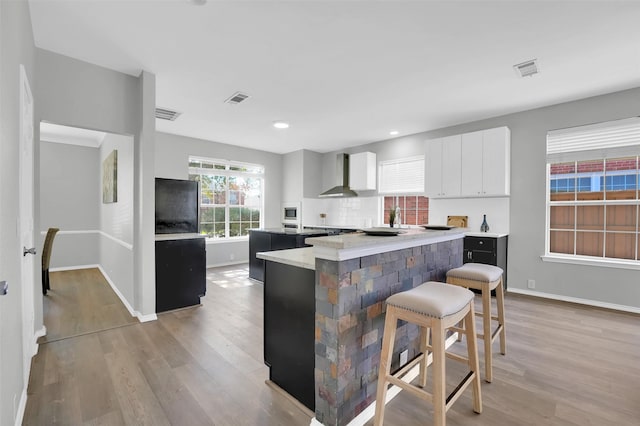 kitchen featuring a kitchen bar, light wood-style flooring, wall chimney exhaust hood, and a kitchen island