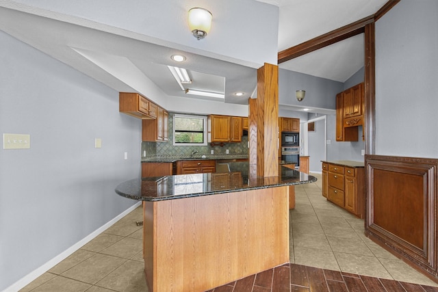 kitchen featuring dark stone counters, light tile patterned floors, decorative backsplash, brown cabinetry, and stainless steel appliances