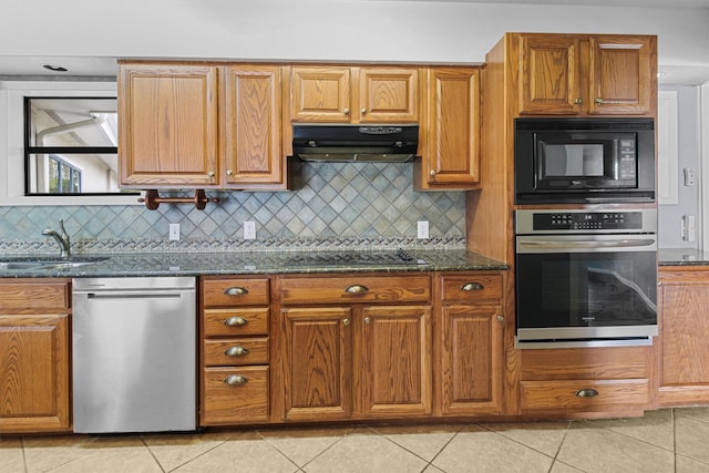 kitchen featuring dark stone countertops, light tile patterned floors, a sink, black appliances, and under cabinet range hood