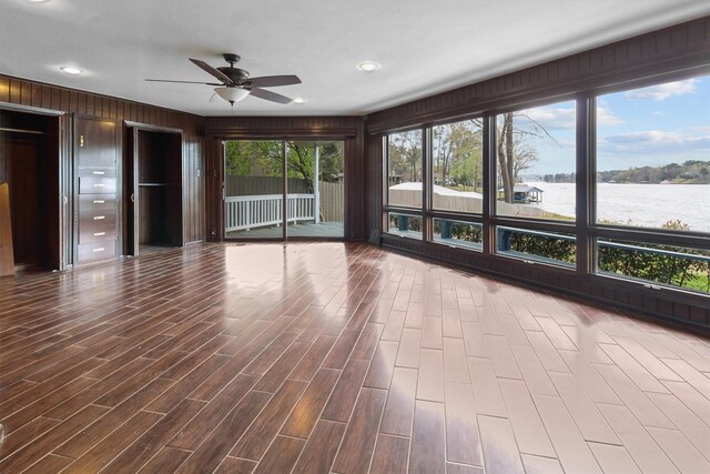 unfurnished living room with dark wood finished floors, a ceiling fan, and a water view