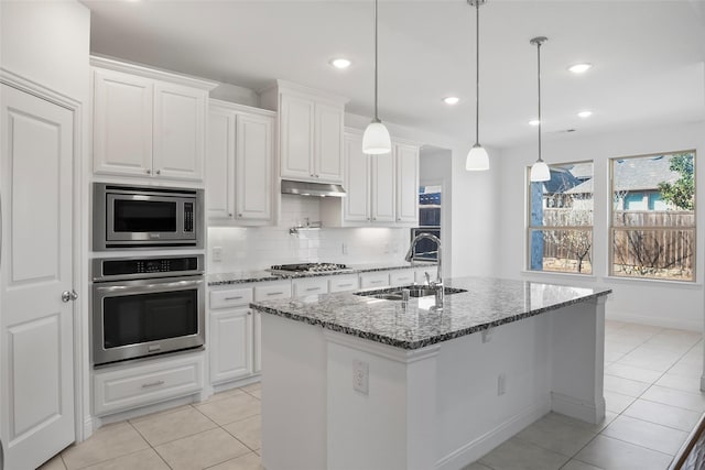 kitchen with a sink, dark stone counters, appliances with stainless steel finishes, light tile patterned floors, and decorative backsplash