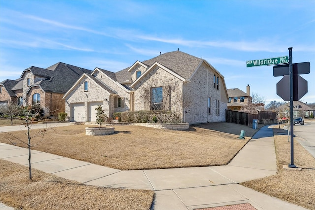 french country style house featuring driveway, fence, a front yard, a garage, and brick siding